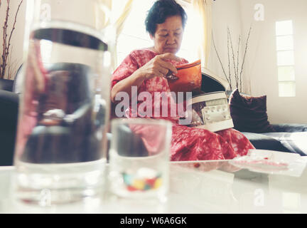 Senior asiatische Frau Pille nehmen Medizin auf der Hand beim Sitzen auf dem Sofa zu Hause Stockfoto