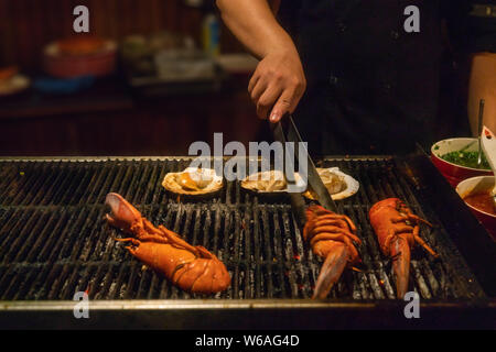 Nahaufnahme einer Hand, die Zangen und grillen Hummer Stockfoto