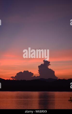 Die Sonne über dem Kra Buri Fluss in Thailand mit Blick auf die Landschaft von Myanmar. Palmwedel fransen oben im Bild Stockfoto