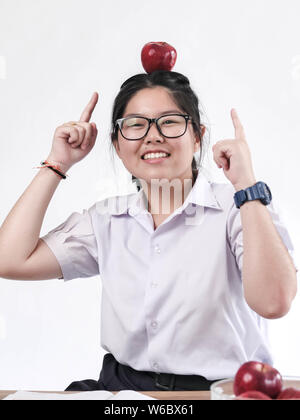 Portrait Of Happy asiatische Schulmädchen in Brillen mit roten Apfel auf den Kopf. Stockfoto