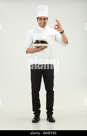 Der Koch hält einen Kuchen und zeigt das Schild OK Stockfoto