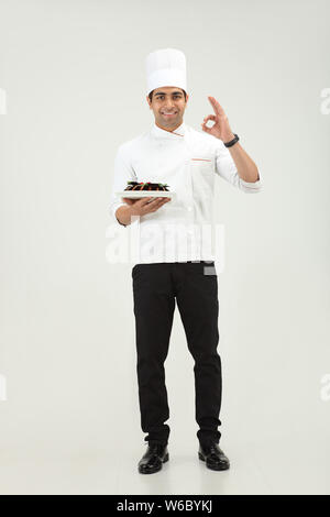 Der Koch hält einen Kuchen und zeigt das Schild OK Stockfoto