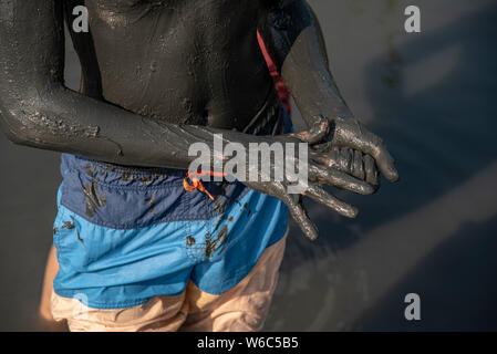 Der Körper und die Arme eines Teenagers, dick mit Schwarzen Heilschlamm verschmiert, haben badeshorts. Wie ein Hintergrund See mit Heilschlamm. Stockfoto
