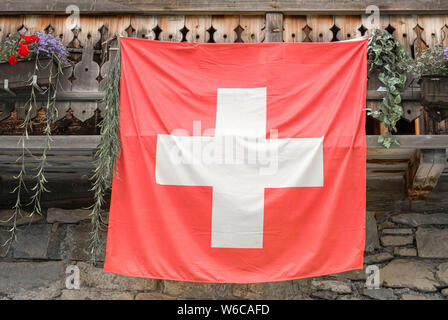 Schweizer Flagge aufhängen auf der Fassade der traditionellen Schweizer Haus bauen. Stockfoto