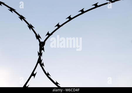 Rostigem Stacheldraht Silhouette am blauen Himmel Hintergrund isoliert. Konzept der Begrenzung, Sicherheit, Gefängnis und Krieg. Stockfoto