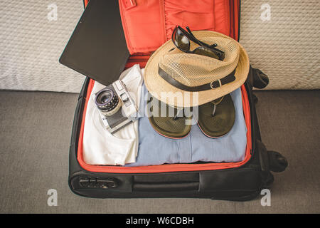 Offene Koffer bereit für Reisen mit Kamera, Tablet, Sonnenbrille und Hut Stockfoto