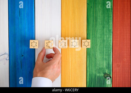 Mann Inverkehrbringen fünf Holzwürfel mit Sternen auf Sie auf farbenfrohen Schreibtisch in einem konzeptionellen Bild. Stockfoto