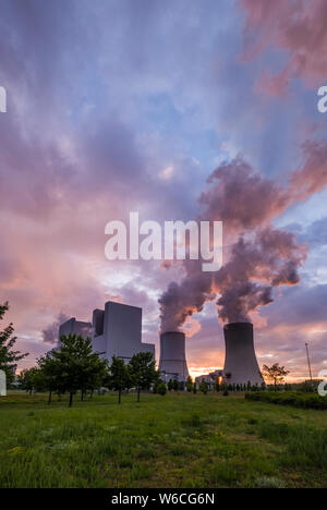 Die Gebäude und dampfende Kühltürme von einem Kohlekraftwerk in der landwirtschaftlichen Landschaft bei Sonnenuntergang Stockfoto