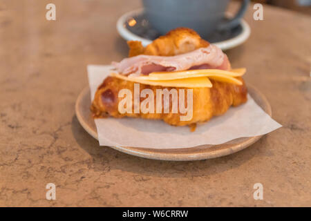 Kontinentales Frühstück mit Croissant und Kaffee. Frisch gebackene Croissant mit Käse, Schinken und Speck gefüllt Stockfoto