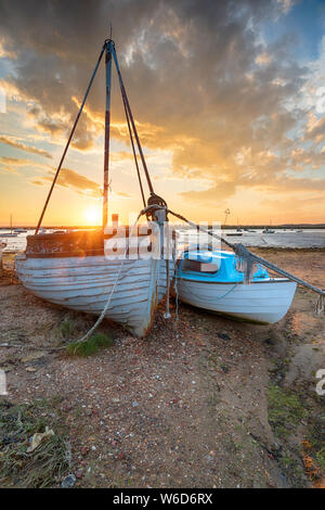Atemberaubenden Sonnenuntergang über dem alten Fischerboote am Strand von West Mersea, ein kleines tidal Insel vor der Küste von Essex Stockfoto