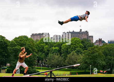 Edinburgh, Schottland, Vereinigtes Königreich, 1. August 2019. Edinburgh Festival Fringe: Die akrobatische Finnische aus Fringe zeigen Super Sonntag durch Race Horse Company mit einem teeterboard, sich in der Luft über die Wiesen mit den Edinburgh Skyline und das Edinburgh Schloss im Hintergrund zu starten. Bild: L bis R Akrobaten Rauli Dahlberg und Jarno Polhuijs Stockfoto