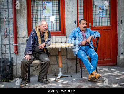 Zwei ältere griechische Männer sitzen im Schatten eines Village Cafe beobachten die Szene. Man hat Sorge, Perlen. Stockfoto