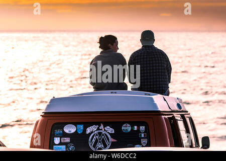 Urlauber sitzen auf ihren VW Volkswagen Wohnmobil einen spektakulären Sonnenuntergang auf den Fistral in Newquay in Cornwall. Stockfoto