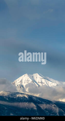 Vertikale schöne Aussicht auf einen Berg mit seiner Spitze bedeckt mit sonnigen weißen Schnee Stockfoto