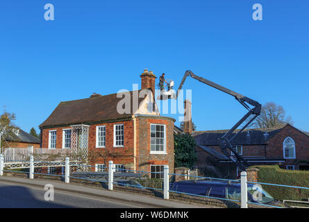 Arbeiter in einer hydraulischen Mann Hebebühne Warenkorb Kran außerhalb ein altes Haus in Hungerford, einer historischen Stadt in Berkshire, England Stockfoto