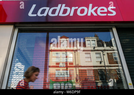 London, Großbritannien. 01 Aug, 2019. Eine Frau geht hinter einem spielende Kommission Geldbußen, Ladbrokes Marke und Logo in London gesehen. Credit: SOPA Images Limited/Alamy leben Nachrichten Stockfoto