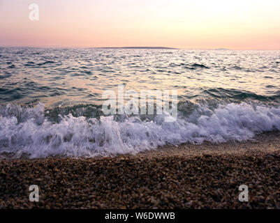 Flutwellen und Sea Foam am Meer und Kieselstrand bei Sonnenuntergang auf der schönen Seenlandschaft Stockfoto
