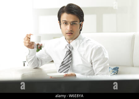 Geschäftsmann beim Fernsehen und bei einer Tasse Kaffee Stockfoto