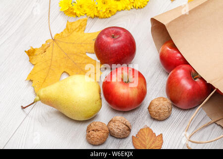 Gelbe Birne, Walnüsse reife, rote Äpfel mit papiertüte auf hölzernen Schreibtisch. Gesunde Bio-lebensmittel. Herbst Thema. Ansicht von oben. Stockfoto