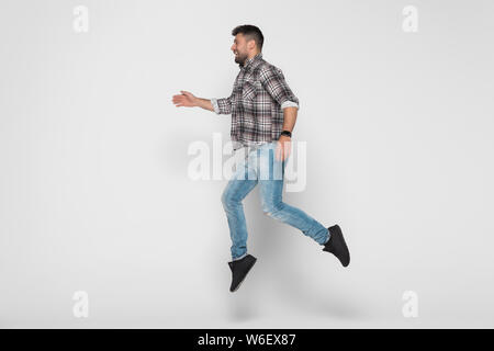 Vertikale Bild von glücklichen Menschen in T-Shirt und Jeans, die in Studio springen. In voller Länge Porträt auf weißem Hintergrund Stockfoto