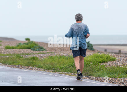 Man joggen entlang einer Küste Straße auf einem schlechten Wetters nassen Tag bei Regen. Stockfoto