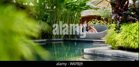 Candid shot der jungen kaukasischen Paar Lounging in modernen Stuhl in der Nähe des luxuriösen Pool von Tropical Hotel und Spa in Bali. Stockfoto