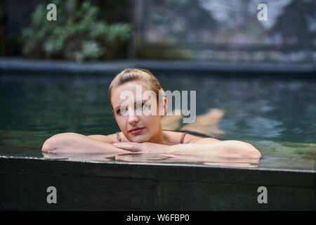 Schöne Frau Entspannung im Freien in einer üppigen und exotischen Stein Schwimmbad luxuriöses Resort im tropischen Urlaub in Bali. Stockfoto