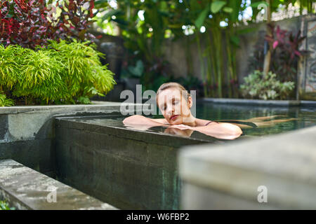 Recht friedliche Frau Entspannung im Freien im sonnigen und Pflanzen umgeben den Pool von luxuriösen Hotel im tropischen Urlaub in Bali. Stockfoto