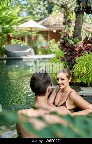 Unposed Schuss romantisches Paar entspannende zusammen in üppigen Resort pool von luxuriösen Hotel in tropischen Bali während der Exerzitien Stockfoto