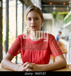 Lifestyle Portrait von selbstbewussten jungen trendigen tausendjährigen Frau mit blonden Haaren sitzen an den hölzernen Tisch in hellen und modernen Restaurant Stockfoto