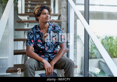 Attraktive hispanic Hipster tausendjährigen business Mann sitzt auf moderne Treppe der helle Zimmer mit tropischen Pflanzen Stockfoto