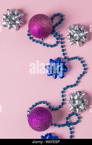 Weihnachten Perlen und Verzierungen auf rosa. Neues Jahr Kugeln, Konfetti. Winterurlaub Vorbereitungen. Ansicht von oben. Minimale festliche Karte. Silber und blauer Schleife mit Stockfoto