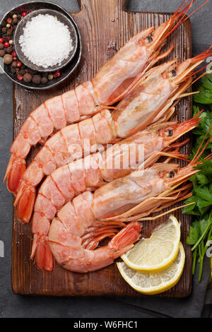 Frische Meeresfrüchte. Langostino Garnelen mit Kräuter und Gewürze auf einem Holzbrett. Ansicht von oben flach Stockfoto