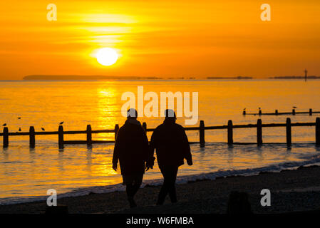 Ein paar einen romantischen Spaziergang Hand in Hand am Strand bei Sonnenuntergang im Herbst in Großbritannien. Stockfoto