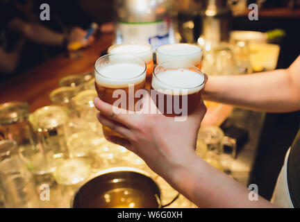 Kellner hält vier Gläser Bier in der Hand in einer Bar oder einem Pub. Biergläser. Stockfoto