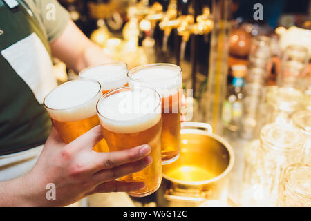 Kellner hält vier Gläser Bier in der Hand in einer Bar oder einem Pub. Biergläser. Stockfoto