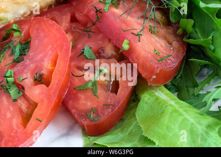 Auf einer Platte drei Scheiben reife rote Tomaten neben einem grünen Salat und Petersilie. In enger vorgestellt. Stockfoto