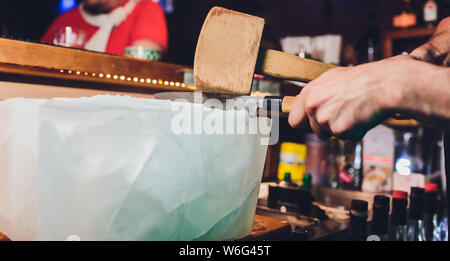 Barkeeper ist ein großer Block aus Eis whiskey Cocktails zubereiten. Selektiver Fokus auf dem Eis. Gastfreundschaft und erlesenen Whiskey Konzept. Stockfoto