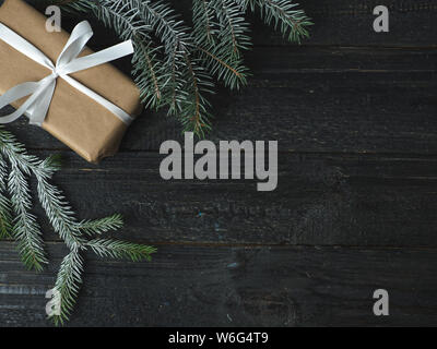 Geschenkbox in Kraftpapier und White Ribbon auf schwarzer Holztisch mit Weihnachtsbaum Niederlassungen Stockfoto