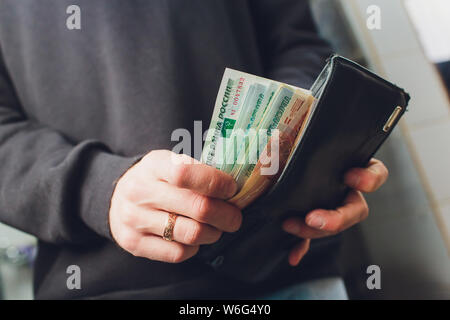 Hände nehmen Sie russische Rubel aus der Brieftasche. Nahaufnahme auf die Hände eines Menschen, wie er ist, eine Banknote aus seiner Brieftasche. Stockfoto