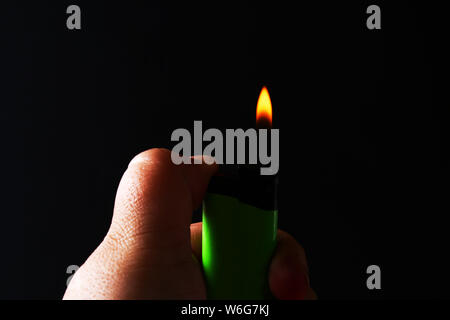 Hand, die brennende Gas Feuerzeuge auf dunklen schwarzen Hintergrund. Tragbares Gerät verwendet eine Flamme zu erstellen. Nahaufnahme Stockfoto