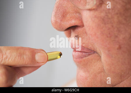 Vitamin- und ergänzen. Nahaufnahme des schönen alten Frau unter gelben Fisch Öl Pille. Weibliche Hand Omega-3-Kapsel in den Mund. Gesunde Ernährung und D Stockfoto