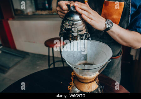 Barista Vorbereitung filter Kaffee im Freien. Männliche barista gießt kochendes Wasser aus dem Wasserkocher Stockfoto