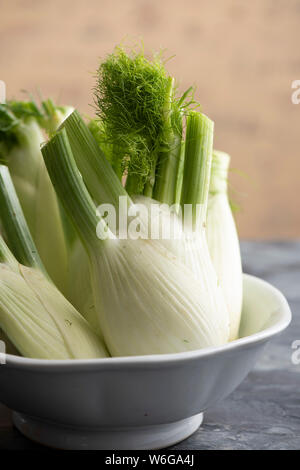 Frische Birnen von Florenz Fenchel arrangiert in einem rustikalen weiße Schüssel auf einer Schiefertafel table top Stockfoto