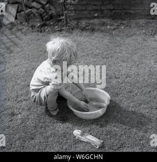 1960, historische, ein kleiner Junge in einem Garten spielt mit seinem Spielzeug Boot im Wasser in ein kleines Becken aus Kunststoff, England, UK. Stockfoto