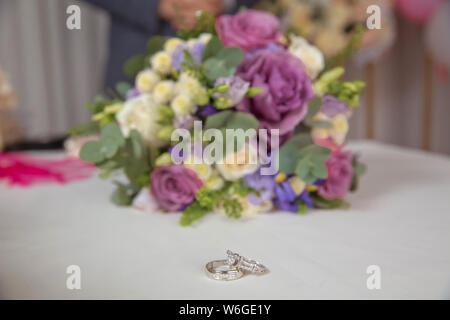 Trauringe und Schönen Blumenstrauß als Braut Zubehör. Schöne getonten Bild mit Verlobungsringe liegen auf einem Holz- Oberfläche gegen die backgrou Stockfoto