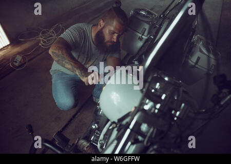 Schön brutalen Mann mit einem Bart Instandsetzung ein Motorrad in der Garage. Stockfoto