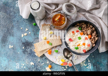 Müsli oder Müsli mit kandierten Früchten in einem dunklen Schüssel, hausgemachtes Joghurt, Orange Marmelade und Milch. Leckeres und gesundes Frühstück. Ansicht von oben Stockfoto