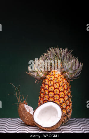 Charakteristische Ananas mit lustigen Top hinter zwei Hälften einer Kokosnuss, die die Äußeren und Inneren weiß braun Shell coco auf einem gemusterten Oberfläche wieder Stockfoto