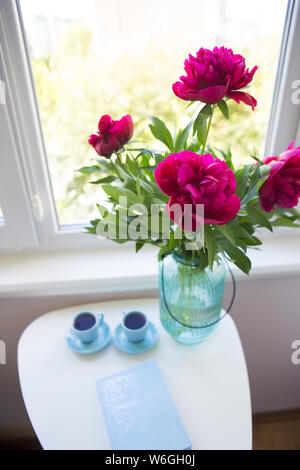 Ein Bouquet von schönen Pfingstrosen und zwei Tassen Kaffee auf einem weißen Tisch Stockfoto